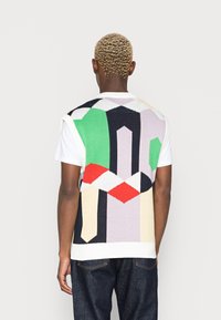 Chaleco de punto con un patrón geométrico multicolor en verde, rojo, negro y crema. Diseño sin mangas con cuello redondo.