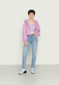 Hoodie cropped em lavanda, top ajustado lilás, jeans retos azul claro e botas de tornozelo azul claro com salto preto.