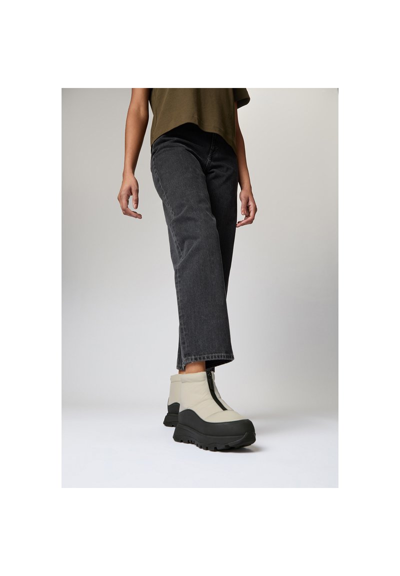 Beige enkellaarsjes met zwarte zolen, met een gestroomlijnde vorm en een ritssluiting aan de voorkant. Gemaakt in combinatie met grijze rechte jeans en een losse top.