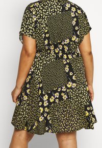 Schwarzes Blumenkleid mit kurzen Ärmeln, das gelbe und lila Blumen in verschiedenen Mustern zeigt. Leichter, fließender Stoff mit elastischem Bund.