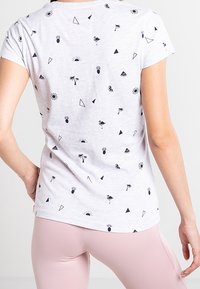 Camiseta de algodón con una base gris claro y patrones tropicales negros que incluyen palmeras, piñas y formas geométricas. Mangas cortas.