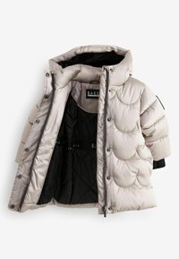 Puffjakke i lys beige med en quiltet skaldesign. Har en høj krave, lynlås lukning og sort foring med tydeligt brandlogo.