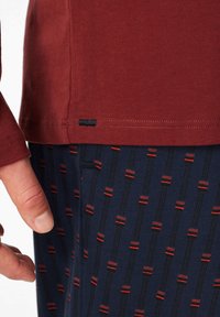 Camicia a maniche lunghe bordeaux con orlo, abbinata a pantaloni blu navy con un motivo a strisce rosse e nere ripetitive. Tessuto morbido in misto cotone.