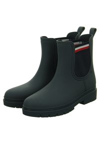 Stivaletti neri impermeabili alla caviglia con una finitura liscia, pannelli elastici laterali in blu navy con strisce rosse e bianche, e una suola in gomma texture.
