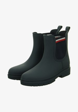 Stivaletti neri impermeabili alla caviglia con una finitura liscia, pannelli elastici laterali in blu navy con strisce rosse e bianche, e una suola in gomma texture.