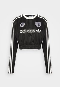 Svart kortärmad Adidas-tröja med lång ärm, vita tre ränder längs ärmarna, vit krage och logopatchar på bröstet.
