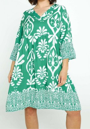 Groene jurk met witte bloemenpatronen, V-hals en driekwart mouwen. Losvallende silhouet met een patroon aan de onderzoom.