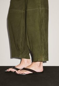 Olivově zelené, semišové culottes s plizé, kombinované s černými plochými žabkami s elegantním designem pásku. Texturovaný a minimalistický vzhled.