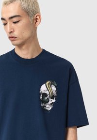 Granatowy bawełniany t-shirt z nadrukiem czaszki oplecionej zielonym wężem, ozdobiony kwiatowymi detalami.