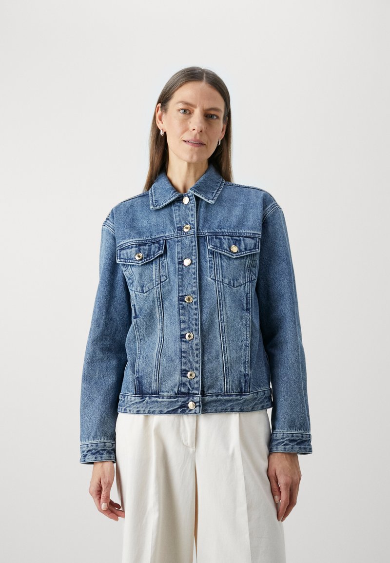 Chaqueta de denim con un lavado azul claro, que presenta un cierre de botones, dos bolsillos en el pecho y un cuello clásico. La tela tiene un acabado ligeramente texturizado.