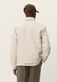 Τζιν μπουφάν σε κρεμ χρώμα με γιακά, μακριά μανίκια και άνετη εφαρμογή, διαθέτει ραφή στην πλάτη και μανσέτες με κουμπιά.