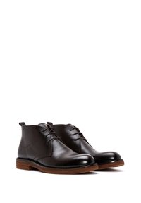 Bottines en cuir marron avec une finition texturée, bouts ronds et deux paires d'œillets pour les lacets. Talons en bois avec un grain subtil.