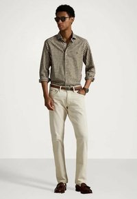 Rudas ir kūno spalvos languotas marškinis su sagomis, šviesiai smėlio spalvos džinsai, rudos odinės diržas, rudi mokasinai ir tamsūs akiniai nuo saulės. Kasdieninis aprangos stilius.