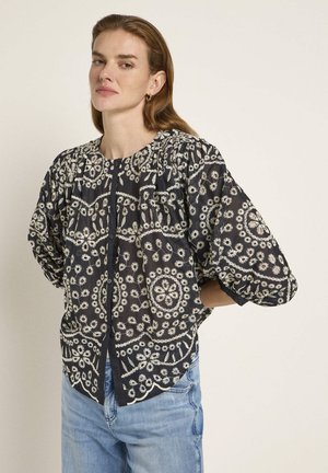Black patterned blouse with white floral embroidery, rounded neckline, gathered details, and balloon sleeves. Paired with light blue jeans.