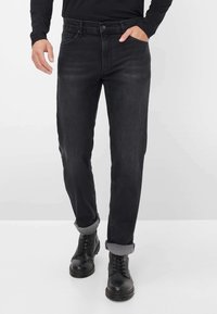 Pantaloni in denim scuro con design a gamba dritta, dotati di chiusura frontale a bottone e orli arrotolati con un bordo texturizzato. Indossati con stivali neri.