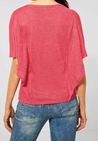 Różowy top z krótkim rękawem o lekkiej, miękkiej fakturze, z okrągłym dekoltem i luźnym, drapowanym fasonem z tyłu. Połączony z dżinsami.