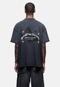 Czarnoszary, oversized T-shirt z graficznym motywem motyla i napisem, z okrągłym dekoltem i krótkimi rękawami. Materiał bawełniany o przetartym wyglądzie.