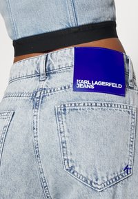 Jeans in denim azzurro chiaro con vita alta, con etichetta blu con la scritta "KARL LAGERFELD JEANS", e due tasche posteriori.