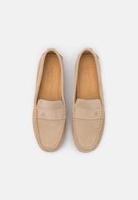 Beige ruskinds loafers med syede detaljer og et lille prægede logo på overdelen. Blød tekstur, rund tå og slip-on design.