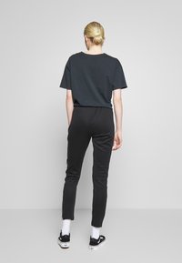 Czarny t-shirt z krótkim rękawem w połączeniu z czarnymi obcisłymi spodniami, zdobionymi subtelnym paskiem z boku; model nosi czarne trampki i białe skarpetki.