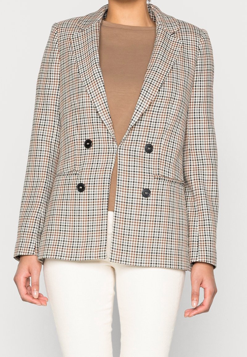 Dwurzędowa marynarka w brązowo-kremowy wzór houndstooth, z czarnymi guzikami, wyraźnie zarysowanymi ramionami oraz dwiema przednimi kieszeniami.