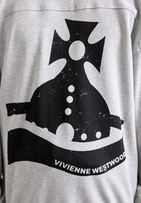 Grå sweatshirt med en stor svart grafik av en kronform med cirkulära accenter och en banderoll som säger "VIVIENNE WESTWOOD."