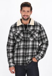 Czarna i biała koszula w kratę flanelowa z miękkim beżowym kołnierzem sherpa, zatrzaskami i dwoma kieszeniami na piersi. Gładki, teksturowany materiał.