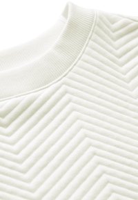 Camicia bianca texturizzata con un colletto a coste e un motivo a zigzag sul tessuto, creando una superficie tattile e visivamente interessante.