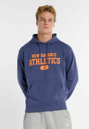 Marineblå hættetrøje med "New Balance Athletics" i orange bogstaver, kængurulomme og ribbede manchetter. Blød stoftekstur.