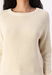 Beige strikket genser med ribbestruktur, med rund hals og raglanlonger. Mykt, middels tungt stoff med avslappet passform.