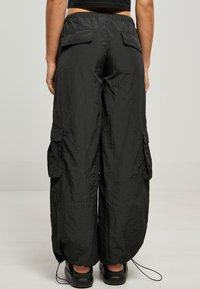 Czarne, lekkie spodnie cargo o zmarszczonej fakturze, z elastycznym pasem i dwiema tylnymi kieszeniami. Posiadają sznurki na dole.