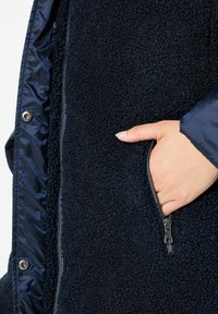 Granatowa polarowa kurtka z gładką podszewką, z zamkniętą kieszenią i teksturowanym wierzchem. Nap w przedniej części dodaje funkcjonalnego akcentu.