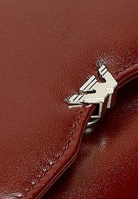 Produkt z czerwonej skóry o błyszczącej, gładkiej fakturze, z srebrnymi elementami metalowymi i detalami przeszycia, które podkreślają jego design i trwałość.