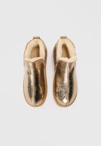 Bottines métalliques dorées à enfiler, avec un intérieur doux et moelleux et un bout arrondi. Présente une couture centrale. Semelle plate de couleur beige.
