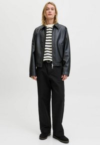 Black faux leather jacket with a collar, zipped front, and side pockets, paired with a striped sweater and black trousers. Textured footwear included.