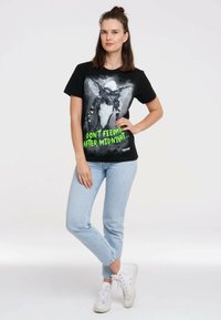 Black cotton t-shirt featuring a gremlin graphic in grayscale and green text that reads, "DON'T FEED ME AFTER MIDNIGHT." Paired with light blue jeans.