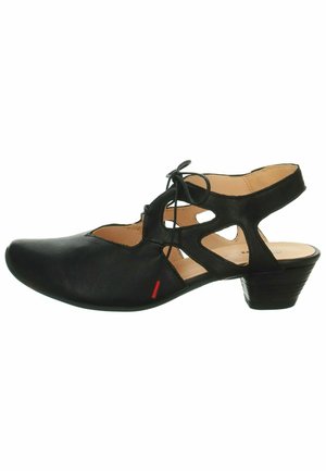 Sandale en cuir noir avec un bout fermé et des motifs découpés, dotée d'un petit talon et d'un laçage à l'avant. Accents rouges près de la semelle.