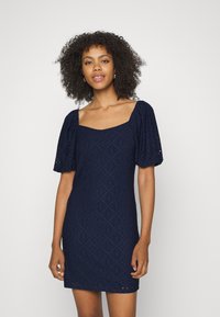 Vestido azul-marinho com decote quadrado, mangas curtas bufantes e um padrão texturizado com recortes bordados.