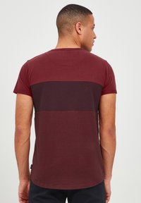 Burgundy short-sleeve T-shirt with a horizontal striped panel design. Smooth texture, round neck, and a straight hem.