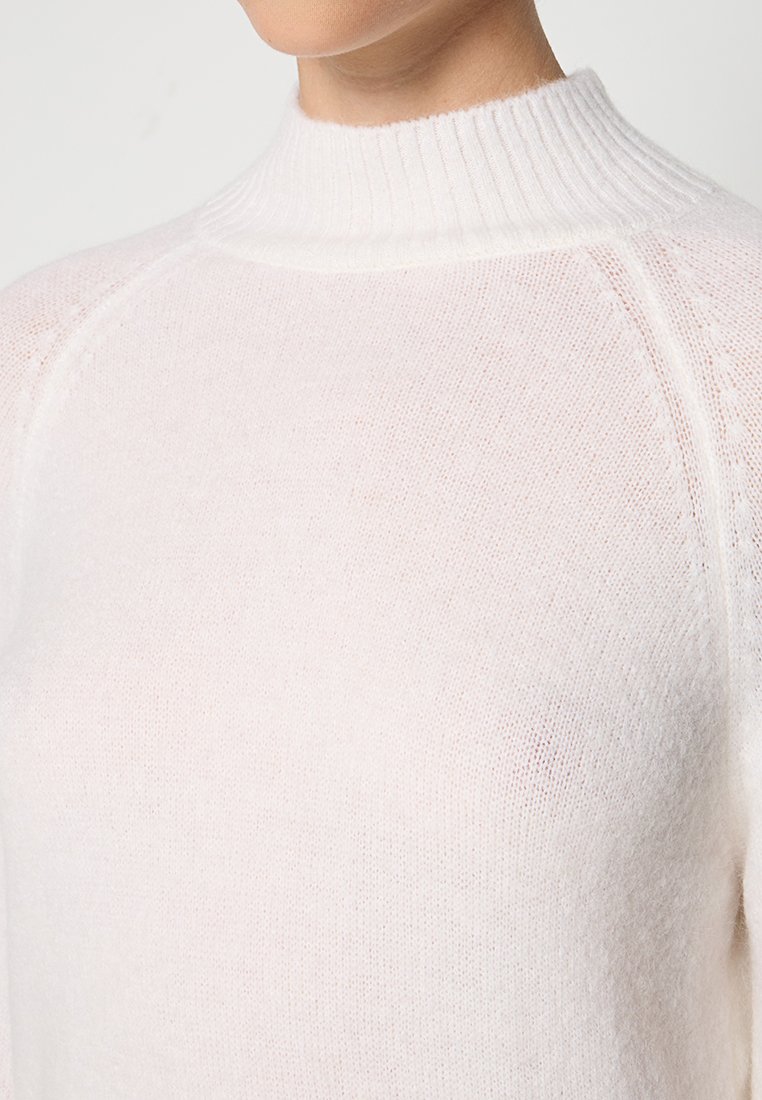 Suéter de punto rosa claro con cuello alto acanalado, corte holgado y una textura fina, con detalles acanalados en el cuello y las costuras.
