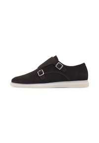 Chaussure slip-on en suede marron foncé avec deux boucles argentées, un bout arrondi et une semelle en caoutchouc blanche contrastante. Texture lisse, design minimal.
