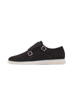 Dunkelbrauner Wildleder-Slipper mit zwei silbernen Schnallen, einer abgerundeten Spitze und einer kontrastierenden weißen Gummisohle. Glatte Textur, minimalistisches Design.
