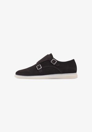 Dark brown suede slip-on shoe featuring two silver buckles, a rounded toe, and a contrasting white rubber sole. Smooth texture, minimal design.