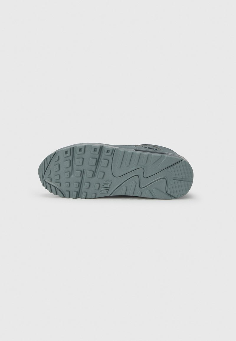 Nike shoe sole in greenish-gray rubber with textured patterns and grooves. Features prominent Nike logo and distinct zigzag design.