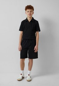Zwarte polo met korte mouwen en bijpassende shorts van textuurstof. Heeft een kraag, een trekkoord in de taille en contrasterende sneakers.