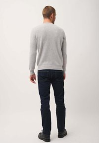 Suéter gris de punto con mangas largas, escote redondo y dobladillo acanalado. Combinado con unos jeans azul oscuro y zapatos negros, visto desde la parte de atrás.