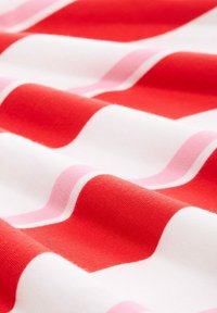 Crvena i bijela tkanina s horizontalnim prugama, koja sadrži teksturirane uzorke različitih širina i mekane, glatke površine.