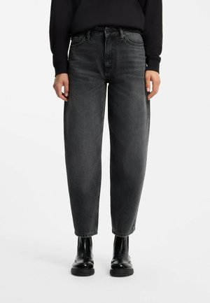Persoon die zwarte, gewassen, losse jeans met een hoge taille draagt, gecombineerd met zwarte leren enkellaarzen en een zwarte top met lange mouwen.