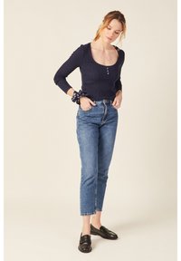 Maglietta a maniche lunghe a coste blu navy con scollatura a barca e dettaglio con bottoni, abbinata a jeans chiari a vita alta e mocassini neri.