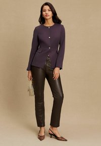 Lilla kohandatud pintsak metallist nööpidega, millele on lisatud pruunid nahast püksid. Aksessuaarideks on hõbedane võrgust käekott ja leopardimustriliste kontsakingadega jalanõud.